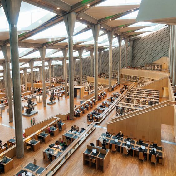 Modern library interior with high ceilings, wooden floors, and rows of study tables and bookshelves.