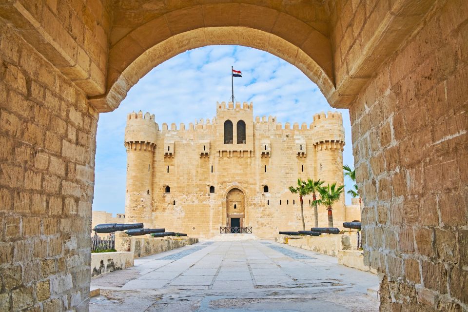 View of a medieval fortress with towers under a blue sky, seen through an arched gateway.