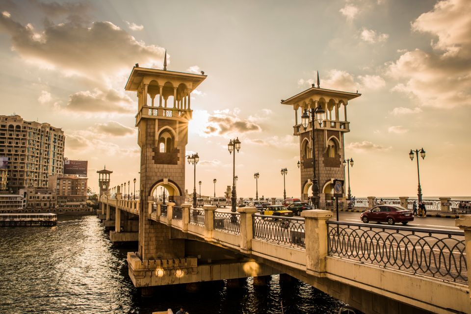 Sunset view of a bridge with twin towers over a waterway, surrounded by buildings under a cloudy sky.