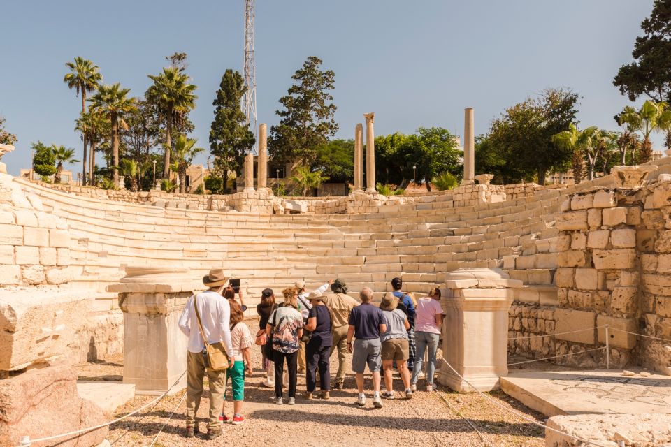 Tourists exploring an ancient amphitheater with stone seats and columns under a clear sky.