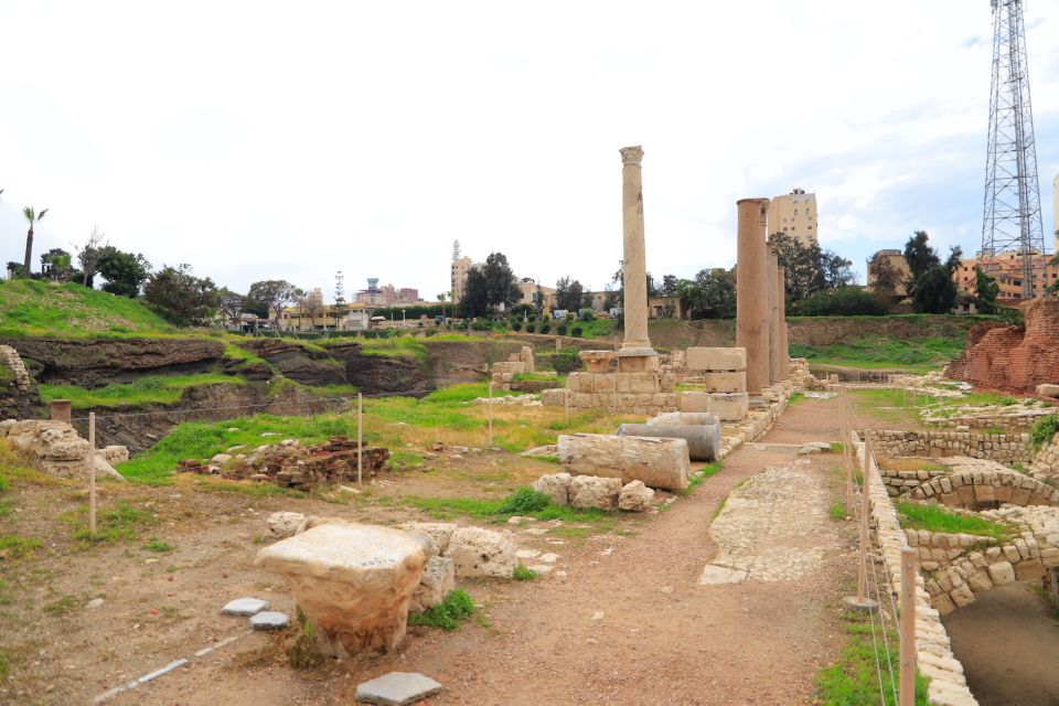 Ancient ruins with columns and pathways, surrounded by urban landscape.