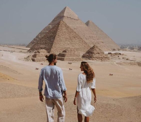 Two people walking towards the Pyramids of Giza in the desert.