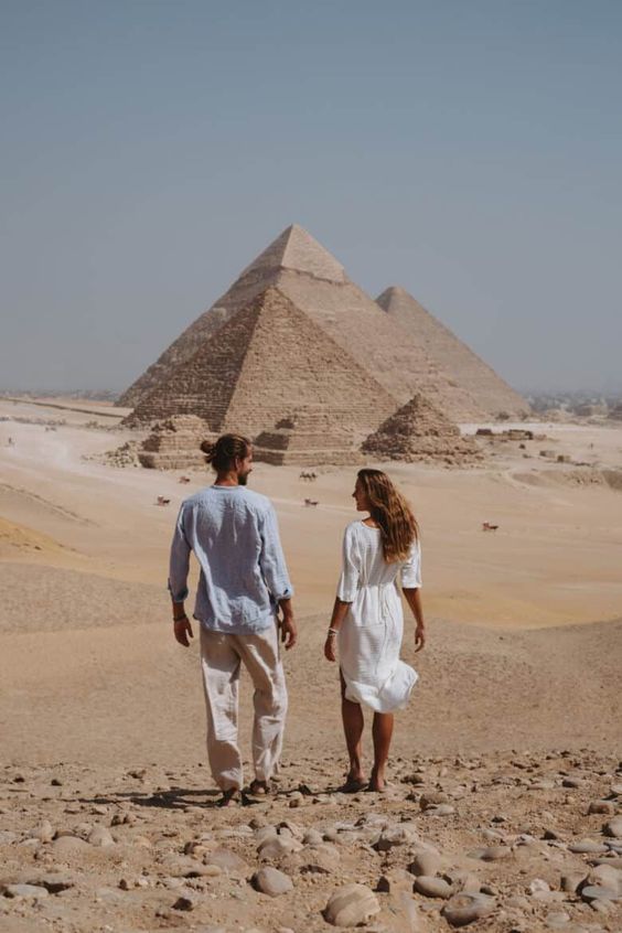 Two people walking towards the Pyramids of Giza in the desert.