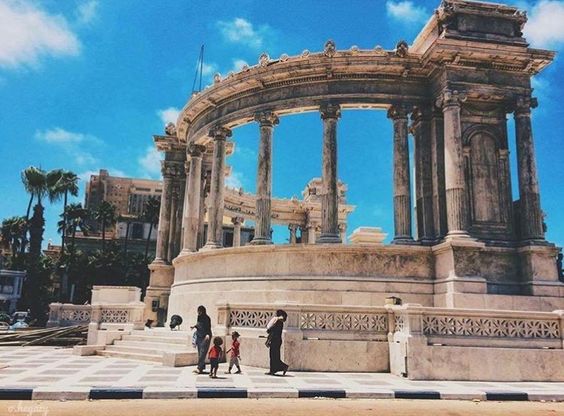 Majestic ancient Roman-style columns against a clear blue sky with people walking in the foreground.