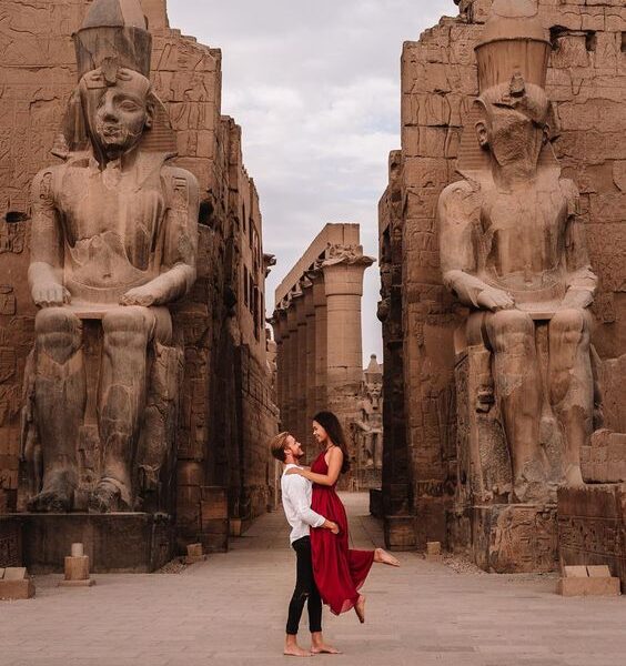 Two people embrace between ancient Egyptian statues.