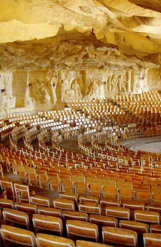 Large underground auditorium with wooden seating and intricate carvings on the cave walls.